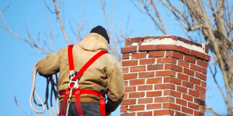 Worker wearing a red harness next to a brick chimney, chimney sweep in Charlotte, NC carried out by the Smoke Alert team