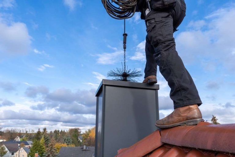 Chimney sweep standing on a roof with a brush above a metal chimney, chimney sweep in Charlotte, NC by Smoke Alert