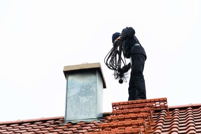 Chimney sweep with brushes on a tiled roof beside a chimney in Charlotte, NC. Home Fire Safety Services Near Me.