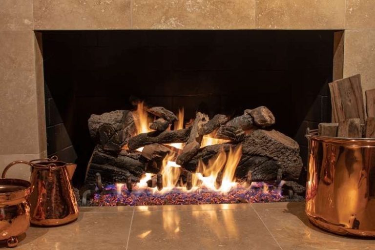 Gas log set burning in a tiled fireplace with copper buckets, Smoke Alert gas log service across Charlotte, NC